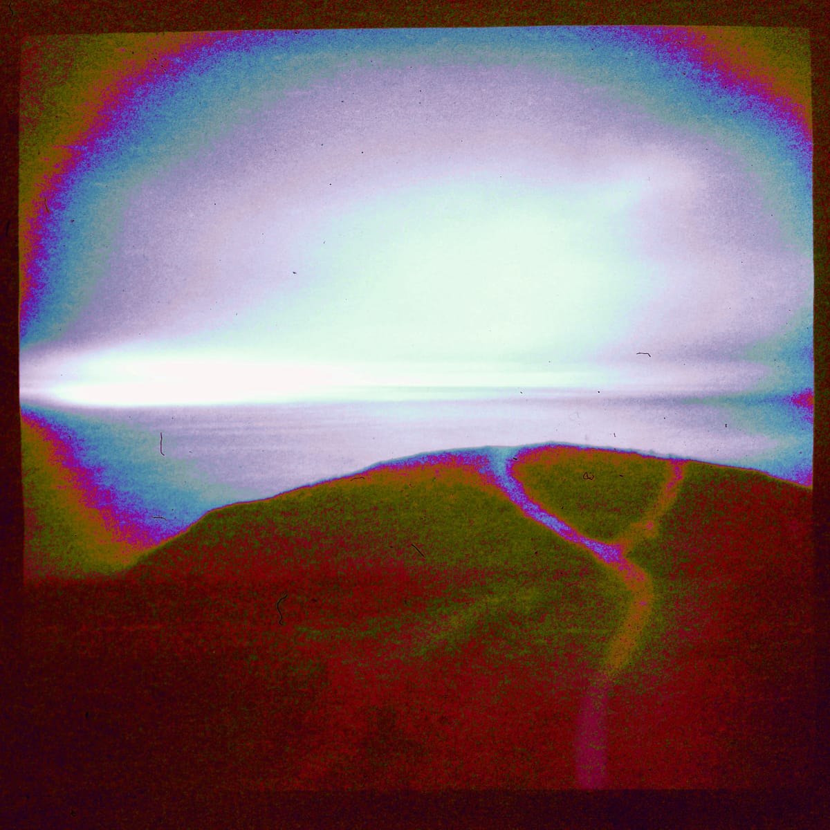 Grainy film photograph of an ocean overlook vista, colorized with unnatural red, magenta, and blue.