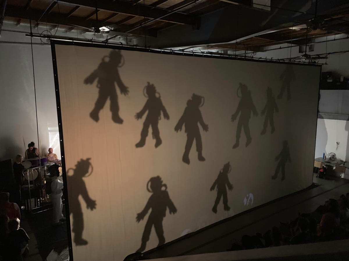 Photo of a shadow puppet screen with several astronauts falling from the sky.