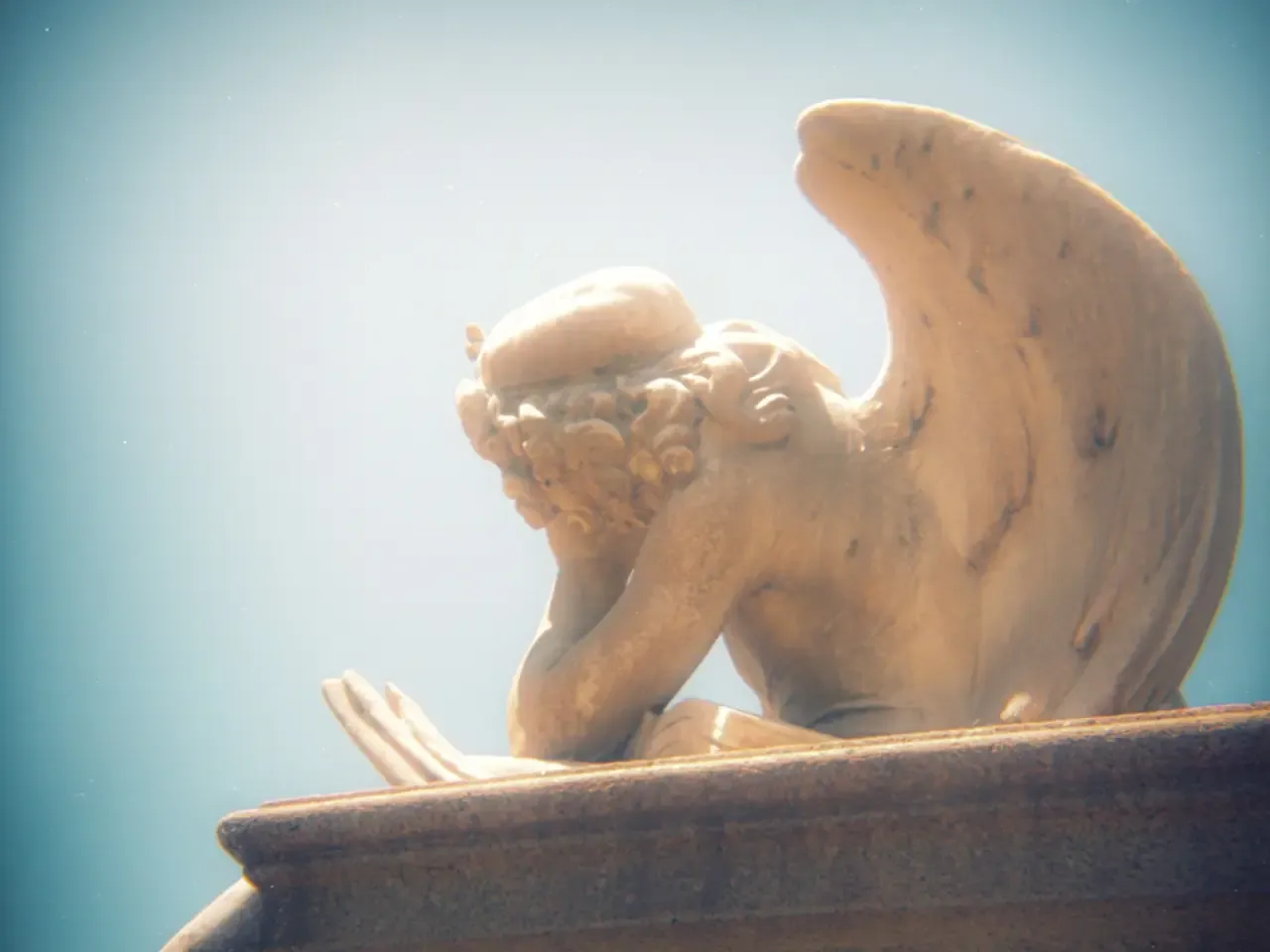soft focus analog photograph of a cemetery angel resting its head in its hand, from behind