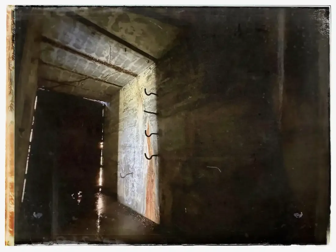 interior of a dark space with rusty and moldy cement walls, dramatic lighting, and metal hooks in the walls
